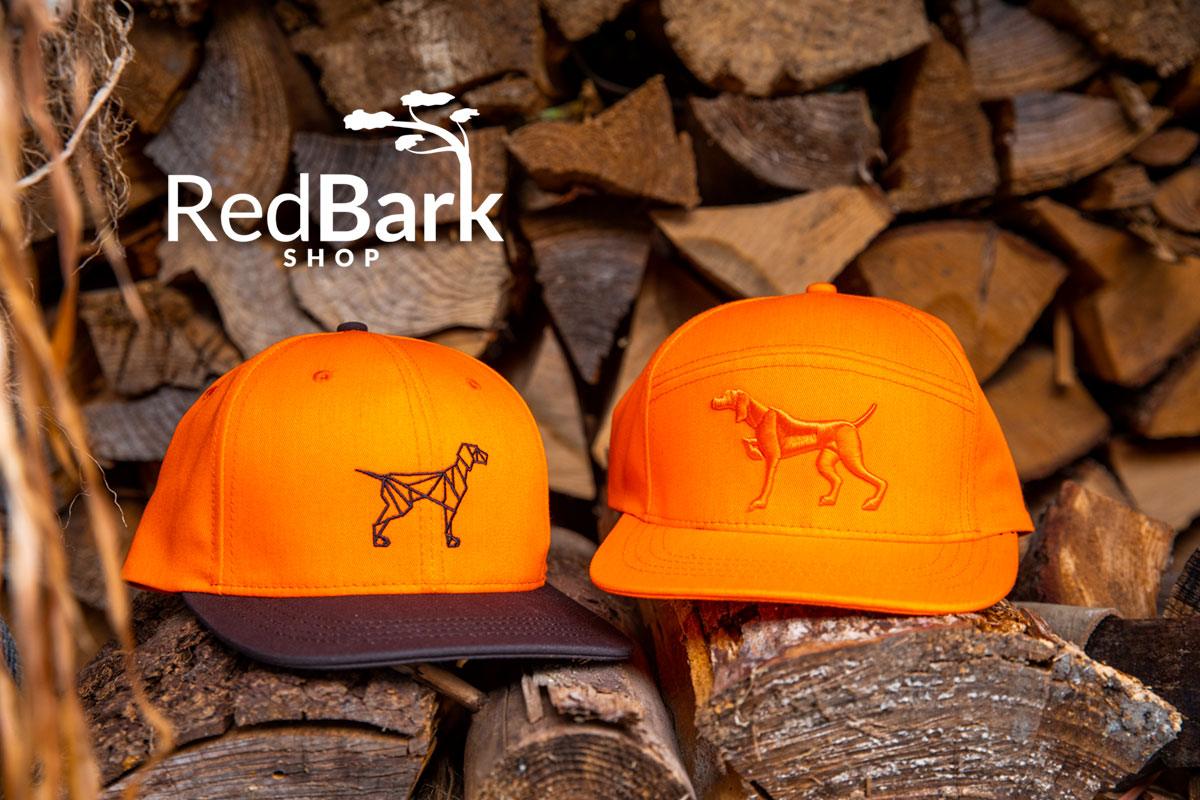 Blaze orange hunting dog hats for pointing dog lovers for field trials placed on logs from Red Bark Shop