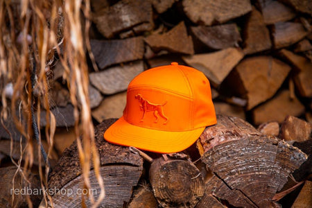 Side view on logs of Blaze orange hunting hat with Puff embroidery Pointer dog